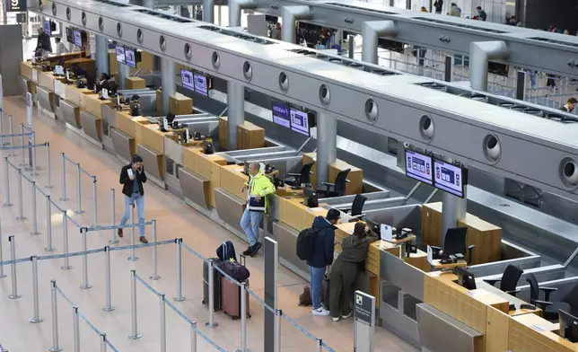 Individuals stand in front of counters at Hamburg Airport, Germany Sunday, March 9, 2025. (Georg Wendt/dpa via AP)