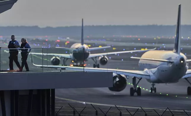 Police officers watch aircrafts take their parking positions at the airport in Frankfurt, Germany, Sunday, March 9, 2025, the evening before a warning strike of all major German airports. (AP Photo/Michael Probst)