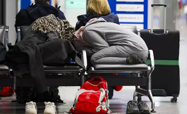 Travelers rest on a bench in the departure terminal at Dusseldorf Airport, Germany Monday, March 10, 2025. (Christoph Reichwein/dpa via AP)