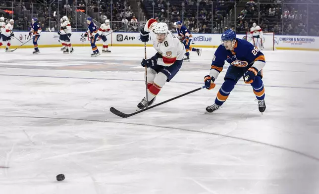 New York Islanders defenseman Alexander Romanov (28) and center Nico Sturm (8) chase the puck during the first period of an NHL hockey game, Sunday, March 16, 2025, in Elmont, N.Y. (AP Photo/Stefan Jeremiah)