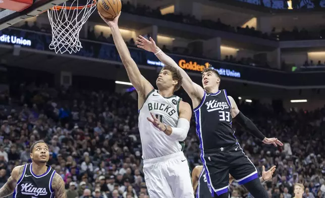 Milwaukee Bucks center Brook Lopez, center, makes a layup as Sacramento Kings forward Jake LaRavia (33) defends during the first half of an NBA basketball game Saturday, March 22, 2025, in Sacramento, Calif. (AP Photo/Sara Nevis)