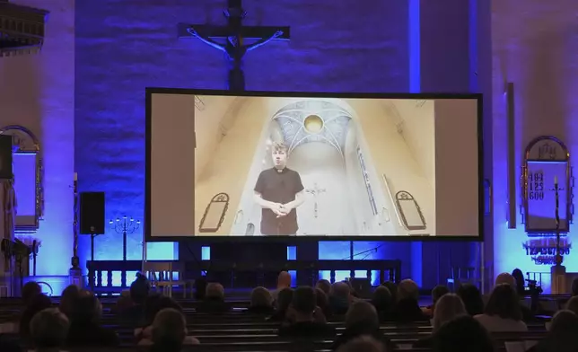 An AI-produced avatar of the Rev. Petja Kopperoinen, on the screen, addresses the attendees of St. Paul's Lutheran church in Helsinki, Finland, Tuesday, March 4, 2025. (AP Photo/Sergei Grits)