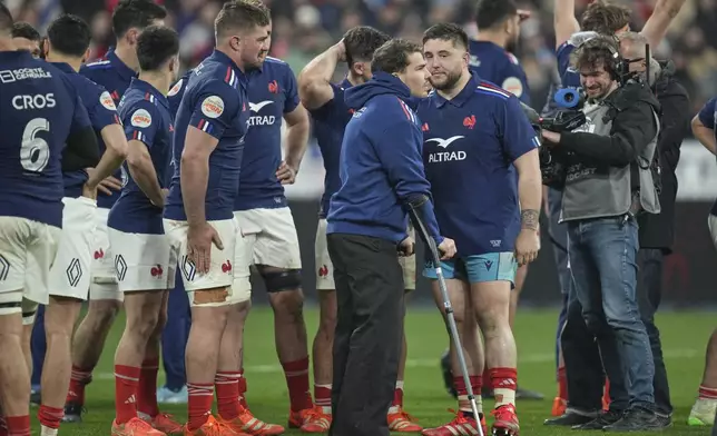 France's Antoine Dupont stands on the pitch on crutches as he celebrates with teammates after the Six Nations rugby union match between France and Scotland at the Stade de France in Saint-Denis, outside Paris, Saturday, March 15, 2025. (AP Photo/Christophe Ena)