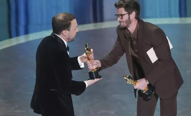 Gints Zilbalodis, left, accepts the award for best animated feature film for "Flow" from Andrew Garfield during the Oscars on Sunday, March 2, 2025, at the Dolby Theatre in Los Angeles. (AP Photo/Chris Pizzello)