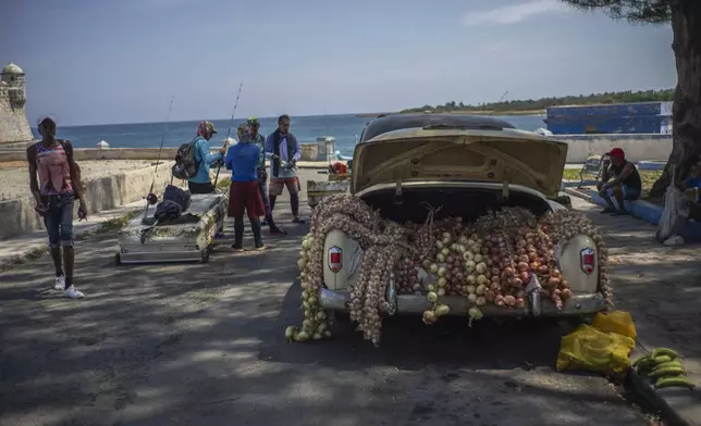 Fishermen talk after a day of fishing on makeshift "corcho" rafts next to a classic American car loaded with garlic and onions for sale in Cojimar, east of Havana, Tuesday, March 25, 2025. (AP Photo/Ramon Espinosa)