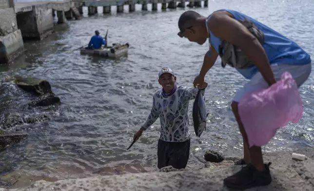 A fisherman hands over the day's catch from a makeshift raft in the water to the shore in Cojimar, east of Havana, Wednesday, March 12, 2025. (AP Photo/Ramon Espinosa)