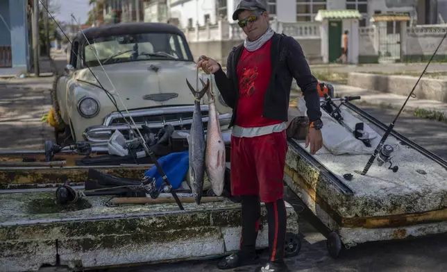 Fisherman nicknamed "El Guajiro" poses for a photo with his catch of the day and his makeshift "corcho" raft in Cojimar, east of Havana, Cuba, Tuesday, March 25, 2025. (AP Photo/Ramon Espinosa)