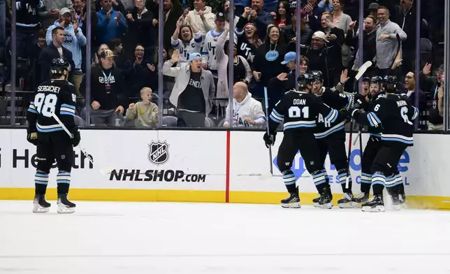 Utah Hockey Club players Utah Hockey Club Mikhail Sergachev (98), Josh Doan (91), John Marino (6), Jack McBain, rear left, Michael Carcone, rear right, celebrate the goal scored by Carcone while Team Owner Ryan Smith pounds on the glass during the second period of an NHL hockey game Monday, March 10, 2025, in Salt Lake City. (AP Photo/Tyler Tate)