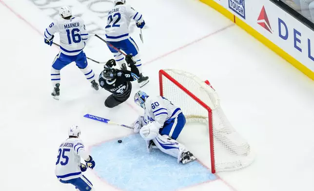 Utah Hockey Club center Clayton Keller (9) is tripped while shooting the puck that was covered by Toronto Maple Leafs goaltender Joseph Woll (60) during the first period of an NHL hockey game Monday, March 10, 2025, in Salt Lake City. (AP Photo/Tyler Tate)