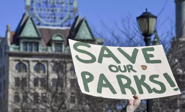 A protester raises a sign that reads "Save Our Parks" under the Scranton Electric City building at a "Save Steamtown" rally to protest the Trump administration layoffs at the Steamtown National Historic Site in Scranton, Pa., Saturday, Feb. 22, 2025. (Aimee Dilger/WVIA via AP)