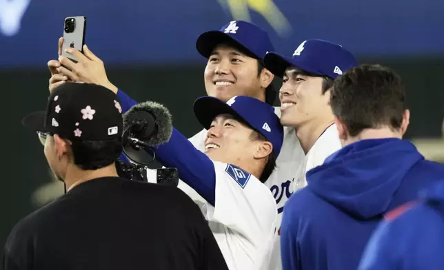 Los Angeles Dodgers starting pitcher Yoshinobu Yamamoto, center, takes a photo with Shohei Ohtani, left rear, and Roki Sasaki, right rear, following the team's MLB Tokyo Series baseball game against the Chicago Cubs in Tokyo, Japan, Wednesday, March 19, 2025. (AP Photo/Hiro Komae)