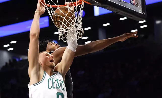 Boston Celtics' Kristaps Porzingis (8) dunks ahead of Brooklyn Nets' Day'Ron Sharpe during the first half of an NBA basketball game, Saturday, March 15, 2025, in New York. (AP Photo/Noah K. Murray)