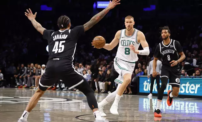 Boston Celtics' Kristaps Porzingis (8) drives to the basket against Brooklyn Nets' Keon Johnson (45) and Ziaire Williams (8) during the first half of an NBA basketball game, Saturday, March 15, 2025, in New York. (AP Photo/Noah K. Murray)