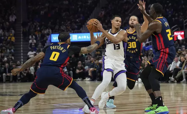 Sacramento Kings forward Keegan Murray (13) moves the ball between Golden State Warriors guards Gary Payton II (0) and Stephen Curry (30) during the first half of an NBA basketball game Thursday, March 13, 2025, in San Francisco. (AP Photo/Godofredo A. Vásquez)