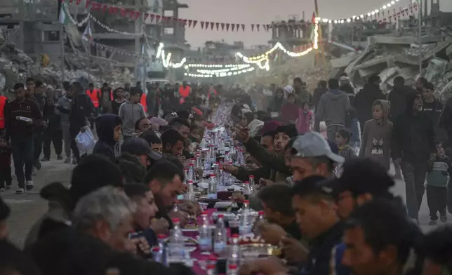 Palestinians sit at a large table surrounded by the rubble of destroyed homes and buildings as they gather for iftar, the fast-breaking meal, on the first day of Ramadan in Rafah, southern Gaza Strip, Saturday, March 1, 2025 (AP Photo/Abdel Kareem Hana)