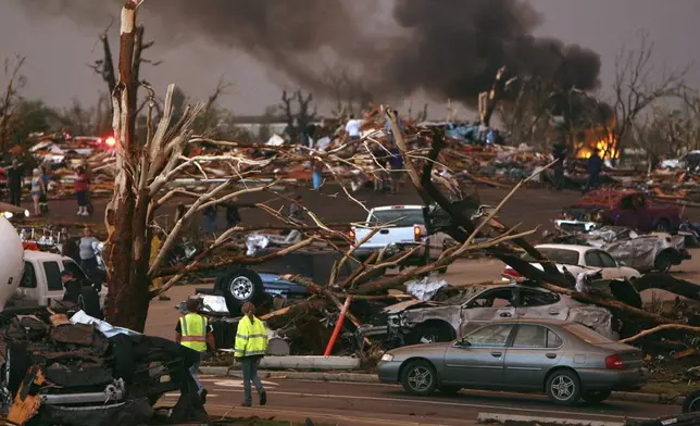 FILE- In this May 22, 2011 file photo, emergency personnel walk through a severely damaged neighborhood after a tornado hit Joplin, Mo. (AP Photo/Mark Schiefelbein, File)