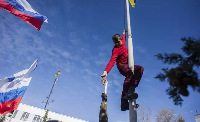 FILE - A member of a pro-Russian self-defense force reaches for a knife to take down a Ukrainian navy flag at the Ukrainian naval headquarters in Sevastopol, Crimea, March 19, 2014. (AP Photo, File)