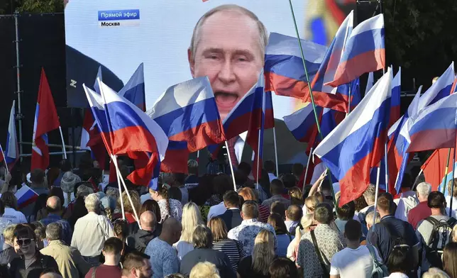 FILE - People watch as Russian President Vladimir Putin delivers a speech after signing treaties for four regions of Ukraine to join Russia in the Moscow's Kremlin, during a meeting in Sevastopol, Crimea, on Sept. 30, 2022. (AP Photo, File)