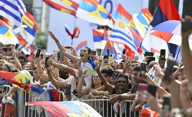 People greet Uruguay's newly sworn-in President Yamandu Orsi and Vice President Carolina Cosse as they ride past in an open car, on Inauguration Day in Montevideo, Uruguay, Saturday, March 1, 2025. (AP Photo/Santiago Mazzarovich)