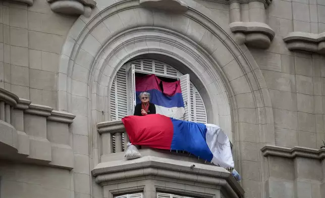 A woman stands on a balcony looking out at people gathering in Independent Square where President-elect Yamandu Orsi will receive the presidential sash, on Inauguration Day in Montevideo, Uruguay, Saturday, March 1, 2025. (AP Photo/Matilde Campodonico)