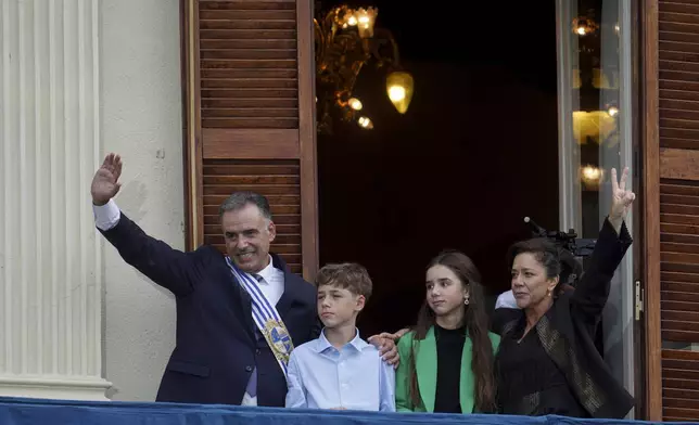 Uruguay's newly sworn-in President Yamandu Orsi and first lady Laura Alonso Perez wave from an Estevez Palace balcony, accompanied by their children, Victorio and Lucia, on Inauguration Day in Montevideo, Uruguay, Saturday, March 1, 2025. (AP Photo/Matilde Campodonico)
