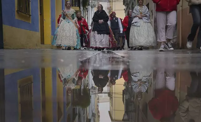 Women dressed in 18th- and 19th-century clothing, known as falleras, are seen reflected in a puddle of rainwater, during the Fallas festival in Valencia, Spain, on Wednesday, March 19, 2025. Five months after deadly floods ravaged Valencia, the Spanish city will host its biggest celebration of the year: Las Fallas. Sculptures were built using wreckage from peoples' homes and lampoon politicians accused of mishandling the catastrophe. (AP Photo/Alberto Saiz)