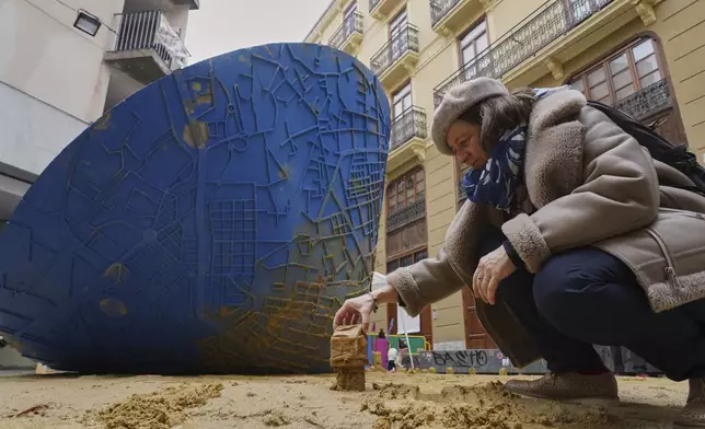 An assistant places sand moulds next to a funnel-shaped sculpture that, as it turns on itself, draws on the ground a map of the towns affected by floods, during the Fallas festival in Valencia, Spain, on Wednesday, March 19, 2025. Five months after deadly floods ravaged Valencia, the Spanish city will host its biggest celebration of the year: Las Fallas. Sculptures were built using wreckage from peoples' homes and lampoon politicians accused of mishandling the catastrophe. (AP Photo/Alberto Saiz)