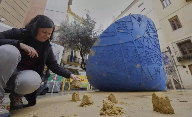 An assistant places sand moulds next to a funnel-shaped sculpture that, as it turns on itself, draws on the ground a map of the towns affected by floods, during the Fallas festival in Valencia, Spain, on Wednesday, March 19, 2025. Five months after deadly floods ravaged Valencia, the Spanish city will host its biggest celebration of the year: Las Fallas. Sculptures were built using wreckage from peoples' homes and lampoon politicians accused of mishandling the catastrophe. (AP Photo/Alberto Saiz)