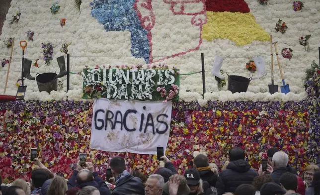 Assistants take photos at a figure of the Virgin decorated with a floral mantle, in honor of those who died during the past floods, during the Fallas festival in Valencia, Spain, on Wednesday, March 19, 2025. (AP Photo/Alberto Saiz)