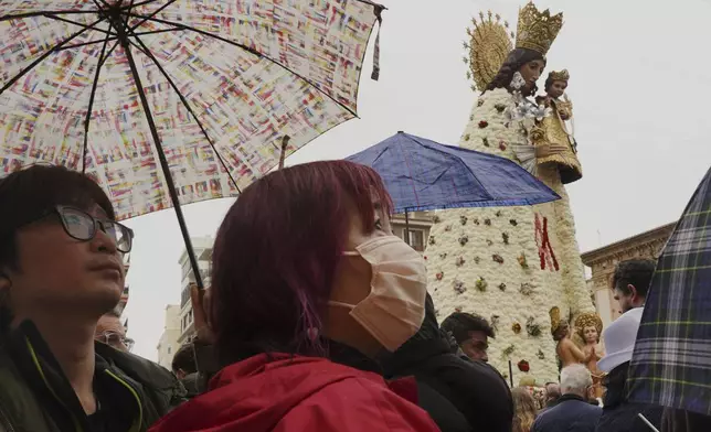 Tourists look at a figure of the Virgin decorated with a floral mantle, in honor of those who died during the past floods, during the Fallas festival in Valencia, Spain, on Wednesday, March 19, 2025. (AP Photo/Alberto Saiz)