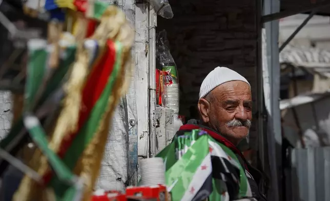 An elderly Druze man stands near Syria's new flag and the multi-colored flag of the Islamic offshoot in Al Karama Square where daily protests took place for over a year in the city of Sweida, Syria, March 4, 2025.(AP Photo/Omar Sanadiki)