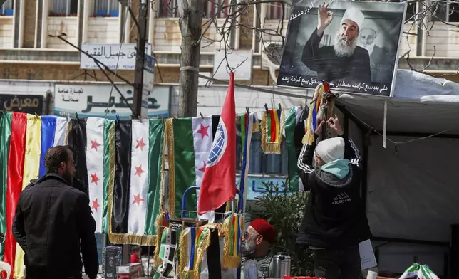 A Druze boy hangs the Islamic offshoot's flag at a newsstand near a poster of spiritual leader Sheikh Hikmat al-Hajari at Al Karama square in the city of Sweida, southern Syria, March 4, 2025.(AP Photo/Omar Sanadiki)