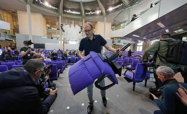 Media surround a worker as he removes a seat during the set-up for the new seating of the federal parliament Bundestag at the Reichstag building in Berlin, Germany, Wednesday, March 19, 2025. (AP Photo/Markus Schreiber)