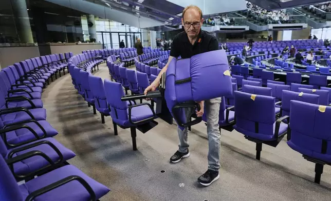 A worker removes a seat during the set-up for the new seating of the federal parliament Bundestag at the Reichstag building in Berlin, Wednesday, March 19, 2025. (AP Photo/Markus Schreiber)