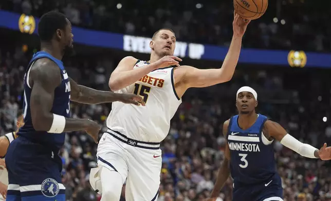 Denver Nuggets center Nikola Jokic, center, passes the ball as he drives between Minnesota Timberwolves forwards Julius Randle, left, and Jaden McDaniels in the first half of an NBA basketball game Wednesday, March 12, 2025, in Denver. (AP Photo/David Zalubowski)
