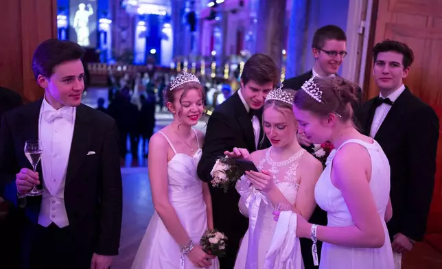 Young people look their phones while waiting to attend the opening ceremony of the Lawyers' Ball in Vienna, Austria, Saturday, March 1, 2025. (AP Photo/Denes Erdos)
