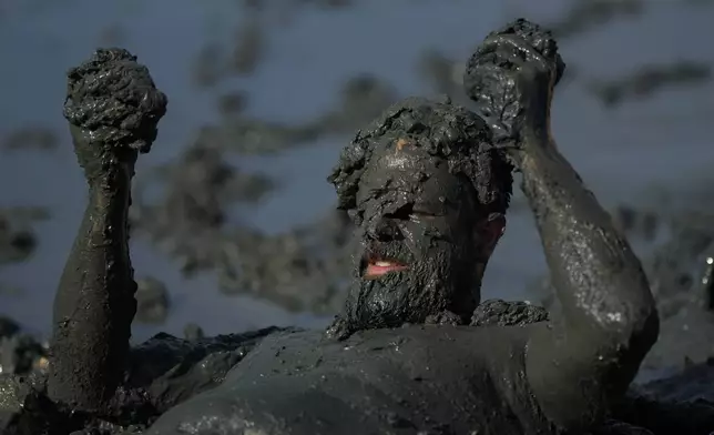 A reveler rolls in the mud during the traditional Mud Block carnival party in Paraty, Brazil, Saturday, March 1, 2025. (AP Photo/Andre Penner)
