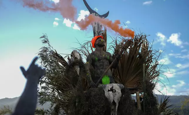 A reveler holds a tiki torch shooting out red smoke during a Mud Block carnival party in Paraty, Brazil, Saturday, March 1, 2025. (AP Photo/Andre Penner)