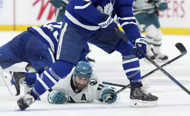 San Jose Sharks forward Luke Kunin (11) is taken down by Toronto Maple Leafs defenseman Conor Timmins, left, during third-period NHL hockey game action in Toronto, Monday, March 3, 2025. (Nathan Denette/The Canadian Press via AP