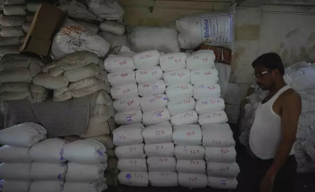 A worker stands next to wrapped bundles of cloth manufactured at a power loom workshop in Bhiwandi, India, Feb. 27, 2025. (AP Photo/Rafiq Maqbool)