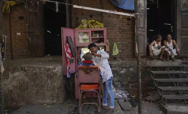 A worker gets his beard trimmed by a barber as others take a break outside a power loom workshop in Bhiwandi, India, Feb. 27, 2025. (AP Photo/Rafiq Maqbool)