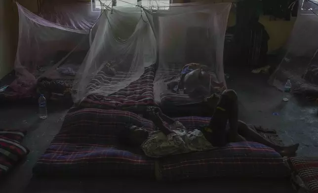 A man sleeps under a mosquito net while another uses his phone in their shared one-room accommodation near a power loom workshop, where they work, in Bhiwandi, India, Feb. 27, 2025. (AP Photo/Rafiq Maqbool)