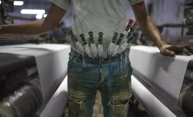 A worker keeps thread bobbins tucked in the waist of his trousers at a power weaving loom workshop in Bhiwandi, India, Feb. 27, 2025. (AP Photo/Rafiq Maqbool)