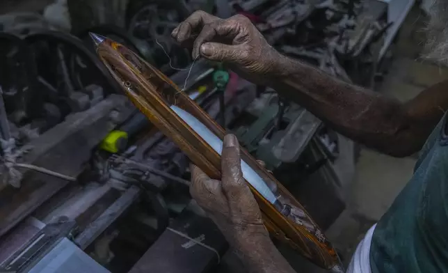 A weaver pulls a length of thread from a shuttle before feeding it to a power weaving loom at a workshop in Bhiwandi, India, Feb. 25, 2025. (AP Photo/Rafiq Maqbool)