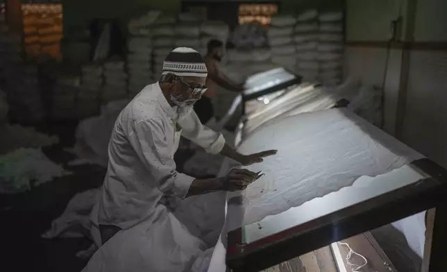 Ghulam Ahmad inspects a sheet of cloth for defects at a power loom workshop in Bhiwandi, India, Feb. 27, 2025. (AP Photo/Rafiq Maqbool)