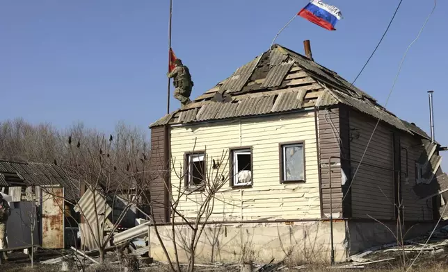 In this photo taken from video distributed by Russian Defense Ministry Press Service on Friday, March 14, 2025, a Russian soldier rises a red flag atop of a house at an area in the Kursk region of Russia after it was taken over by Russian troops. (Russian Defense Ministry Press Service via AP)
