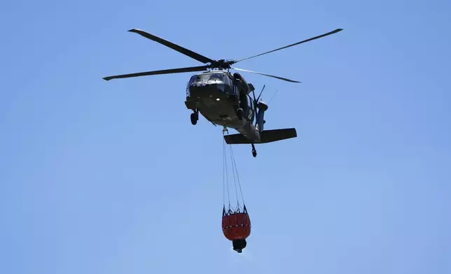 A helicopter carries water to battle the Pauline Road wildfire Thursday, March 20, 2025, in Cleveland, Texas. (AP Photo/David J. Phillip)