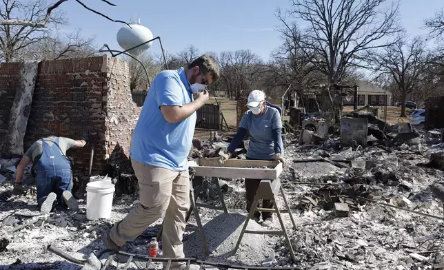 Cayton Jones, front, walks through the ashes that are left of his home in the Hidden Oaks neighborhood in Stillwater, Okla., on Monday, March 17, 2025, after wildfires burned through the area on Friday. (AP Photo/Alonzo Adams)