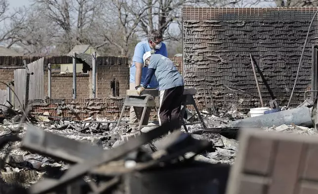 Cayton Jones, left, and his family look through the ashes of his home in the Hidden Oaks neighborhood in Stillwater, Okla., Monday, March 17, 2025, after wildfires burned through the area on Friday. (AP Photo/Alonzo Adams)