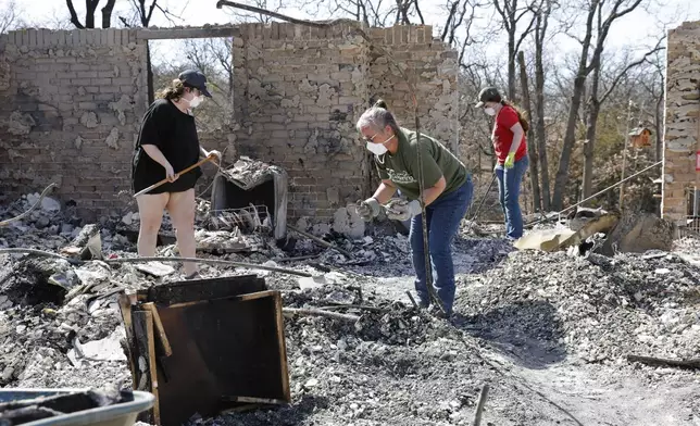 Friends and students of home owner Andrine Shufran, look through the ashes that are left of her home in the Hidden Oaks neighborhood in Stillwater, Okla. on Monday, March 17, 2025 after wildfires burned through the area Friday. (AP Photo/Alonzo Adams)